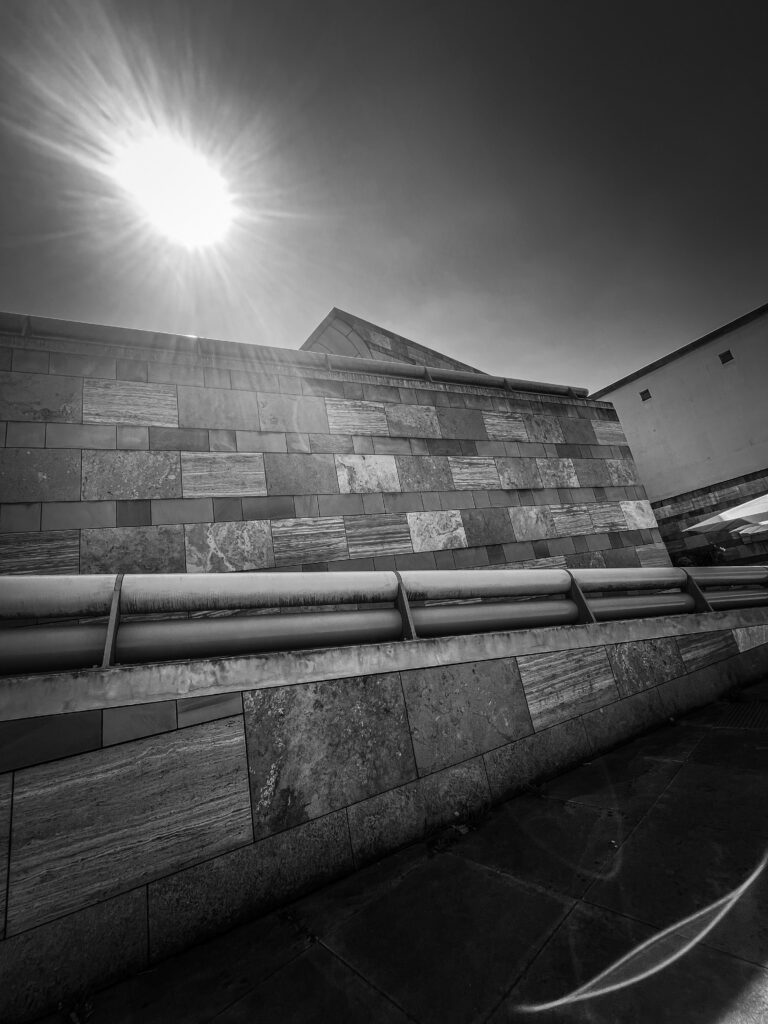 Schwarz-Weiß-Aufnahme der steinernen Außenarchitektur der Staatsgalerie Stuttgart mit strahlender Sonne am Himmel.
