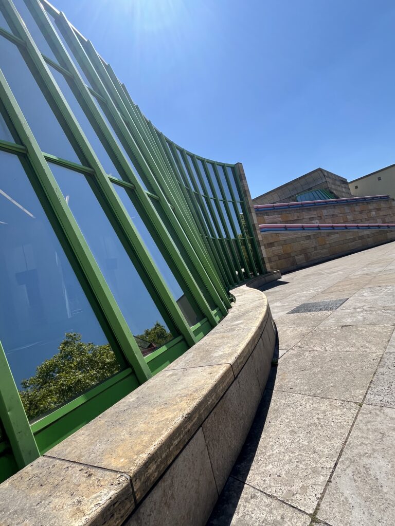 Schräg aufgenommene Außenansicht der Staatsgalerie Stuttgart mit grüner Glasfassade und steinernen Gebäudeteilen.