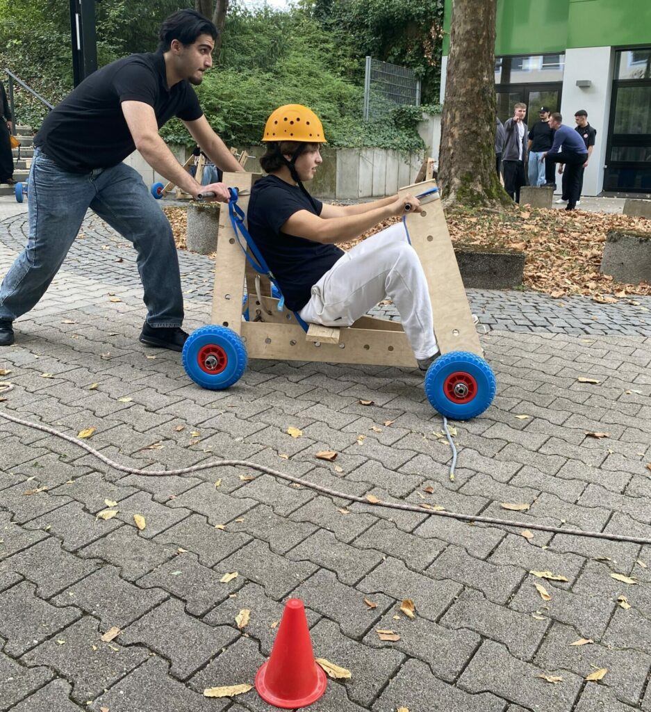 Ein Schüler schiebt die Seifenkiste an, während ein Mitschüler mit Helm am Steuer sitzt.
